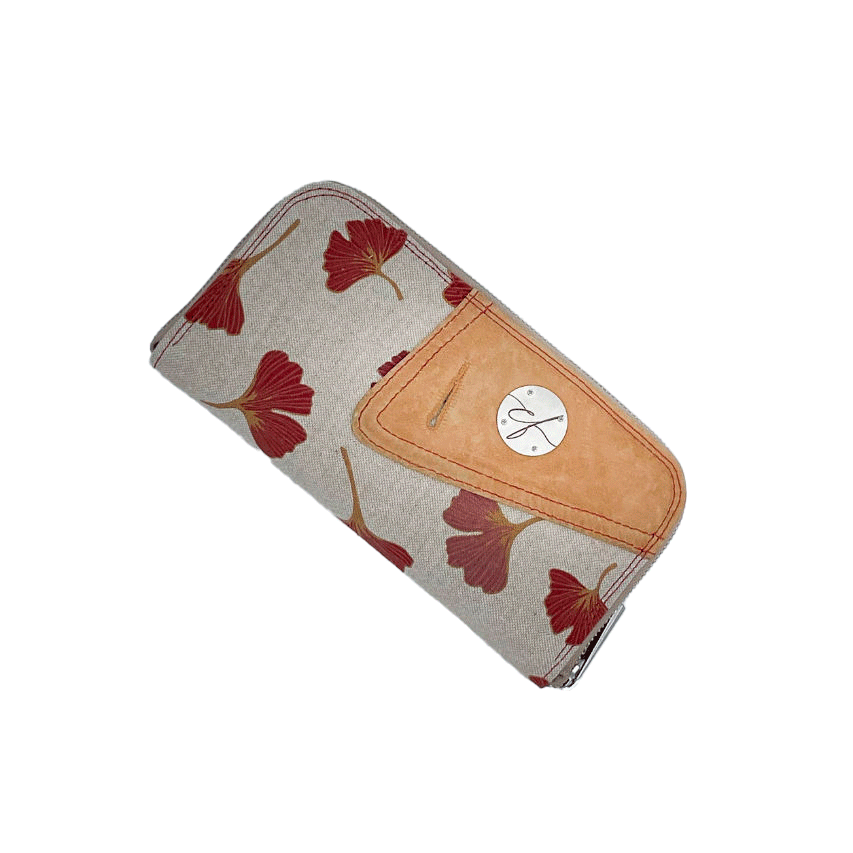 Un porte-cartes-et-monnaie zippé fait de cuir de couleur camel et d'une toile en polycoton avec un motif de feuilles de Ginkgo Biloba rouges.