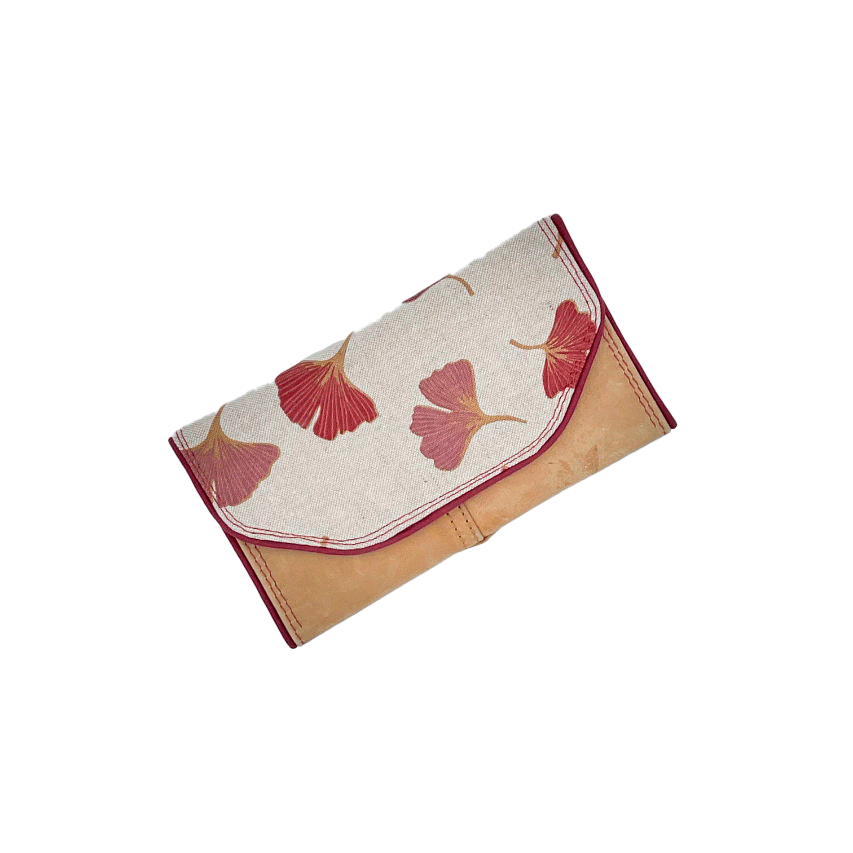 Un portefeuille fabriqué avec du cuir de couleur camel et une toile en polycoton avec un motif de feuilles de Ginkgo Biloba rouges.