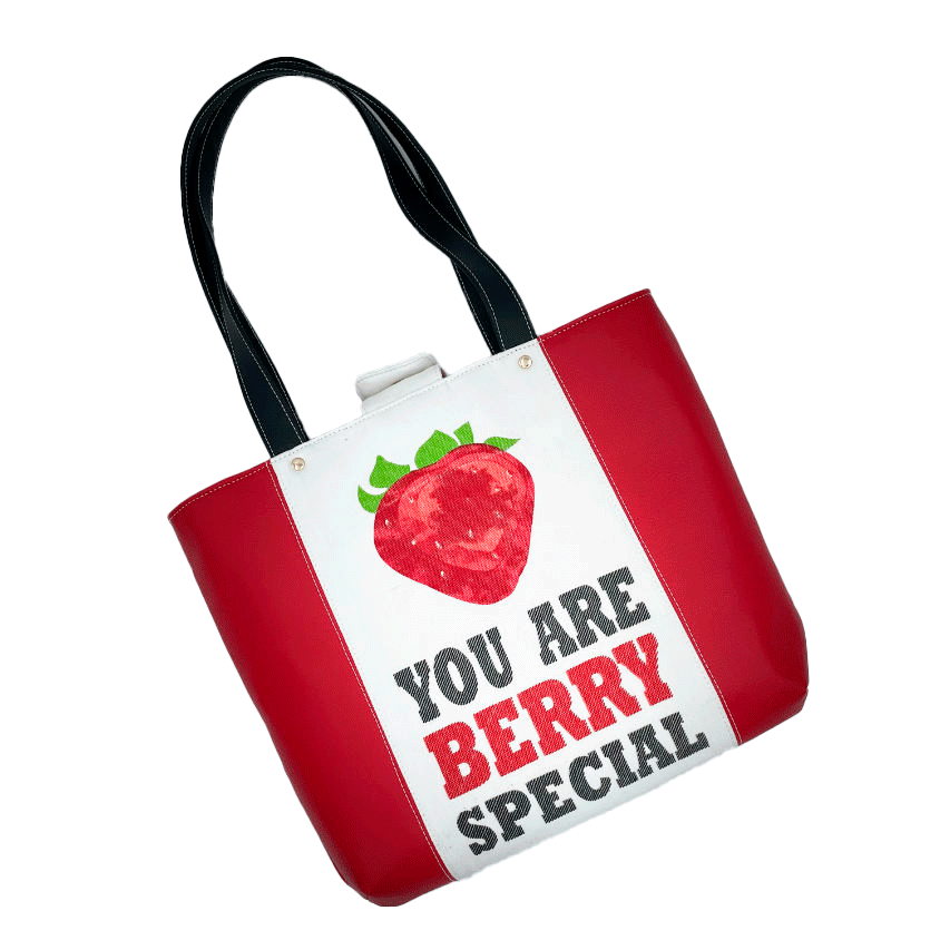 Un grand sac fait à l'extérieur de simili rouge et d'une toile imprimée d'un dessin de fruit avec un jeu de mots en anglais dessous, et à l'intérieur d'une popeline rouge vif.