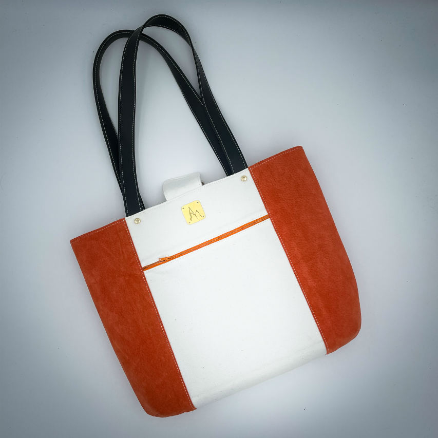 Un grand sac fait à l'extérieur de cuir orange et d'une toile imprimée d'un dessin de fruit avec un jeu de mots en anglais dessous, et à l'intérieur d'une viscose orange irisée.