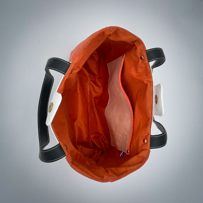 Un grand sac fait à l'extérieur de cuir orange et d'une toile imprimée d'un dessin de fruit avec un jeu de mots en anglais dessous, et à l'intérieur d'une viscose orange irisée.