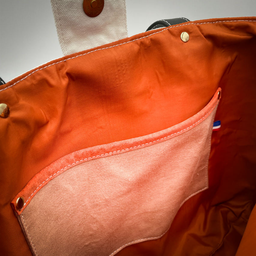 Un grand sac fait à l'extérieur de cuir orange et d'une toile imprimée d'un dessin de fruit avec un jeu de mots en anglais dessous, et à l'intérieur d'une viscose orange irisée.