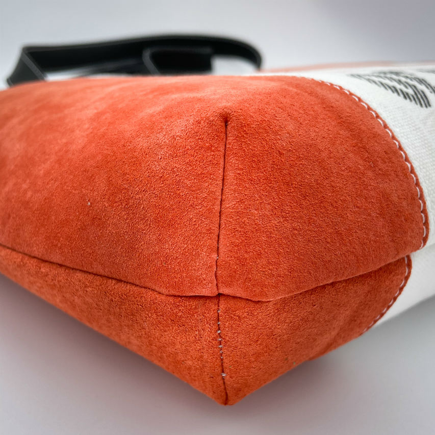 Un grand sac fait à l'extérieur de cuir orange et d'une toile imprimée d'un dessin de fruit avec un jeu de mots en anglais dessous, et à l'intérieur d'une viscose orange irisée.