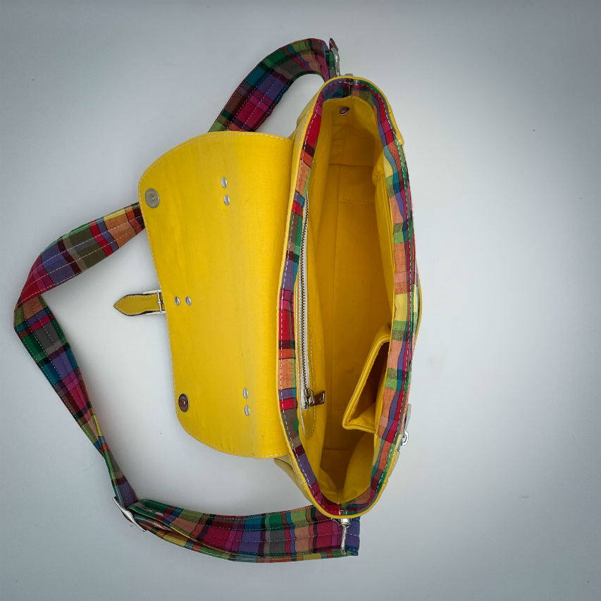 Un sac cartable constitué de cuir jaune et de toile de madras multicolore.