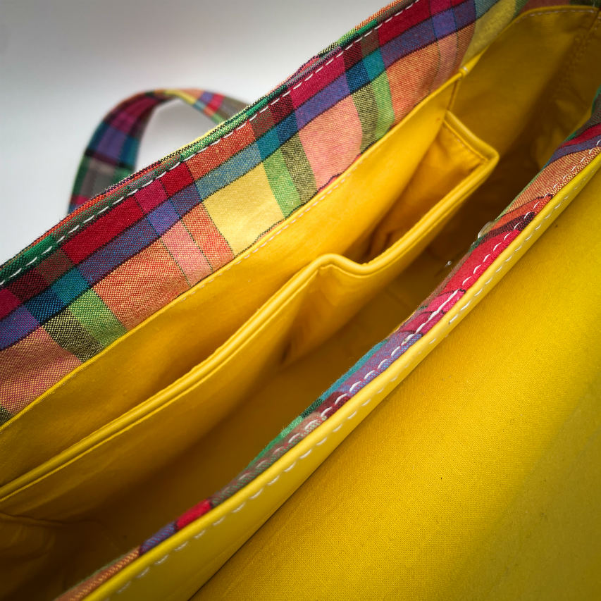 Un sac cartable constitué de cuir jaune et de toile de madras multicolore.