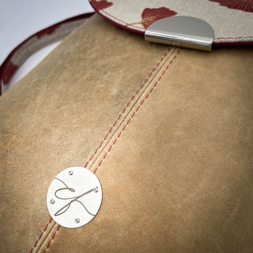 Un sac à dos fait d'un cuir de couleur camel et d'une toile en polycoton avec un motif de feuilles de Ginkgo Biloba rouges.