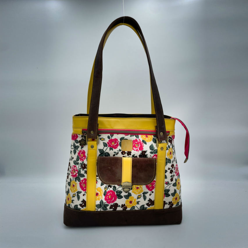 Un sac d'épaule fabriqué à partir de cuirs chocolat et jaune mariés à une toile fleurie avec des fleurs roses et jaunes.