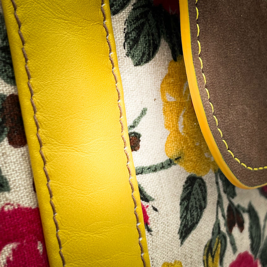 Un sac d'épaule fabriqué à partir de cuirs chocolat et jaune mariés à une toile fleurie avec des fleurs roses et jaunes.