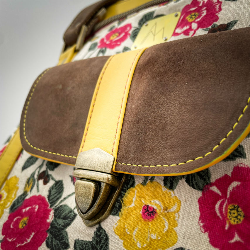 Un sac d'épaule fabriqué à partir de cuirs chocolat et jaune mariés à une toile fleurie avec des fleurs roses et jaunes.