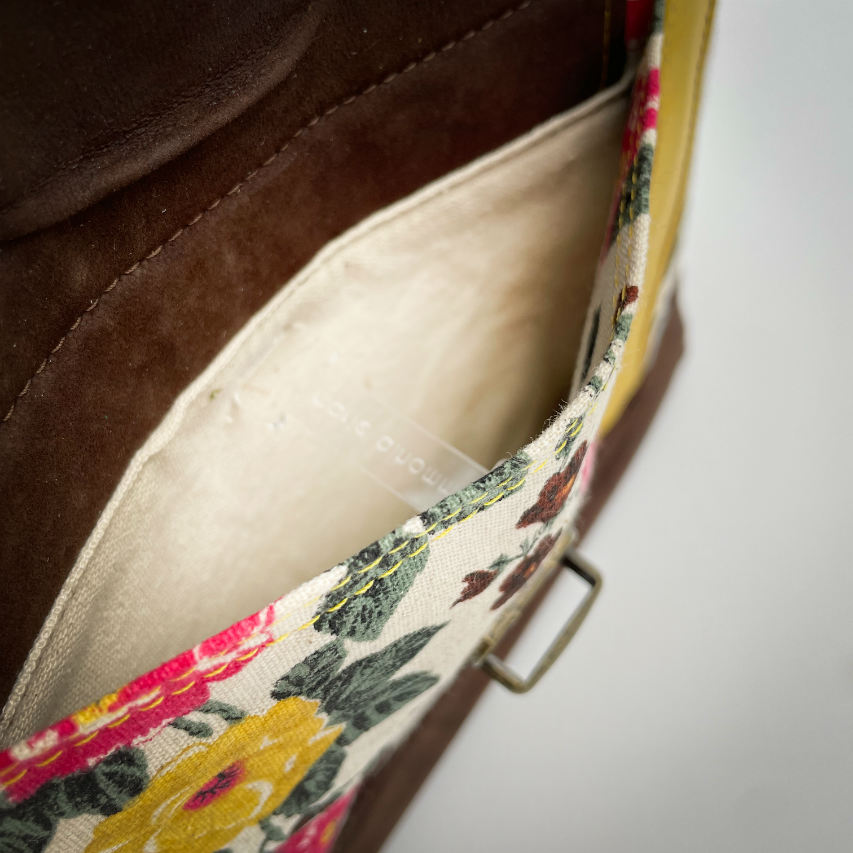 Un sac d'épaule fabriqué à partir de cuirs chocolat et jaune mariés à une toile fleurie avec des fleurs roses et jaunes.