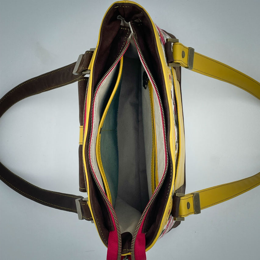 Un sac d'épaule fabriqué à partir de cuirs chocolat et jaune mariés à une toile fleurie avec des fleurs roses et jaunes.