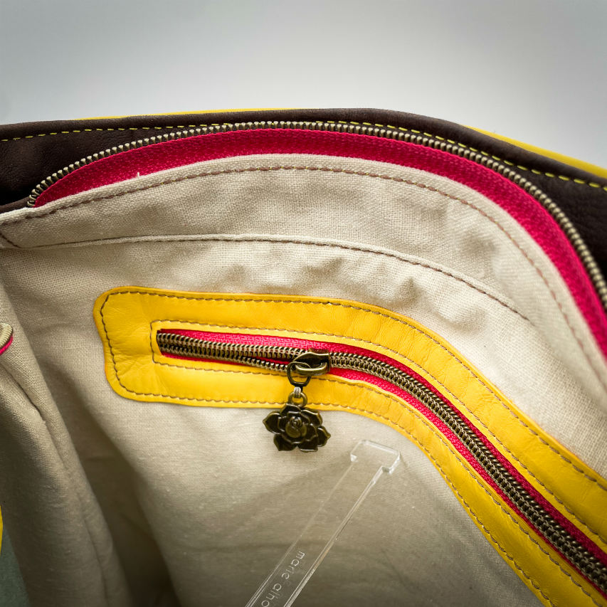 Un sac d'épaule fabriqué à partir de cuirs chocolat et jaune mariés à une toile fleurie avec des fleurs roses et jaunes.