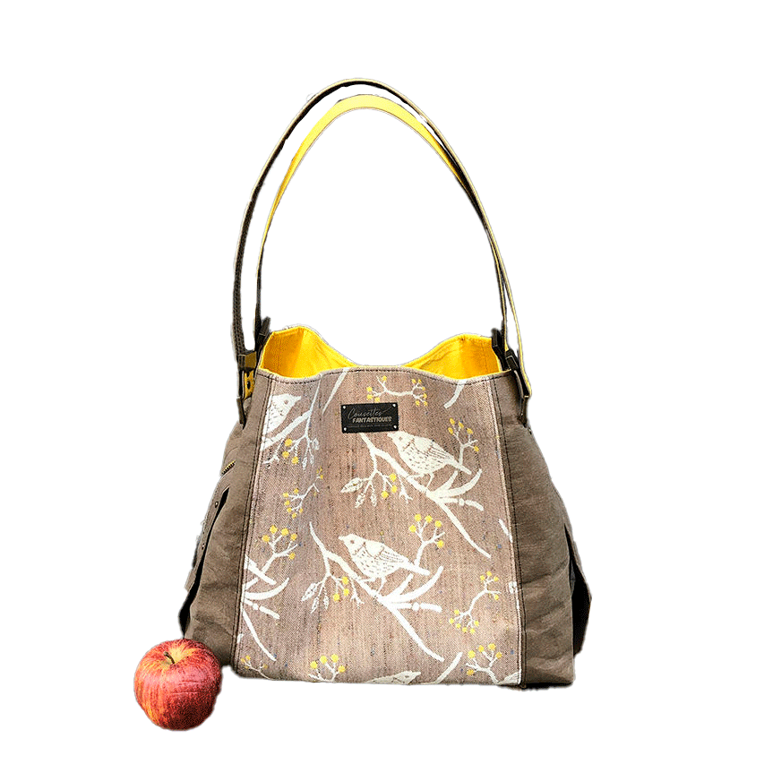 Un sac d'épaule fait à partir de papier lavable couleur chocolat, écharpe de portage beige rosé chiné, au motif d'oiseaux blancs dans des branchages blancs et jaune, avec une doublure jaune vif.