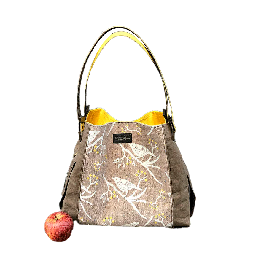 Un sac d'épaule fait à partir de papier lavable couleur chocolat, écharpe de portage beige rosé chiné, au motif d'oiseaux blancs dans des branchages blancs et jaune, avec une doublure jaune vif.