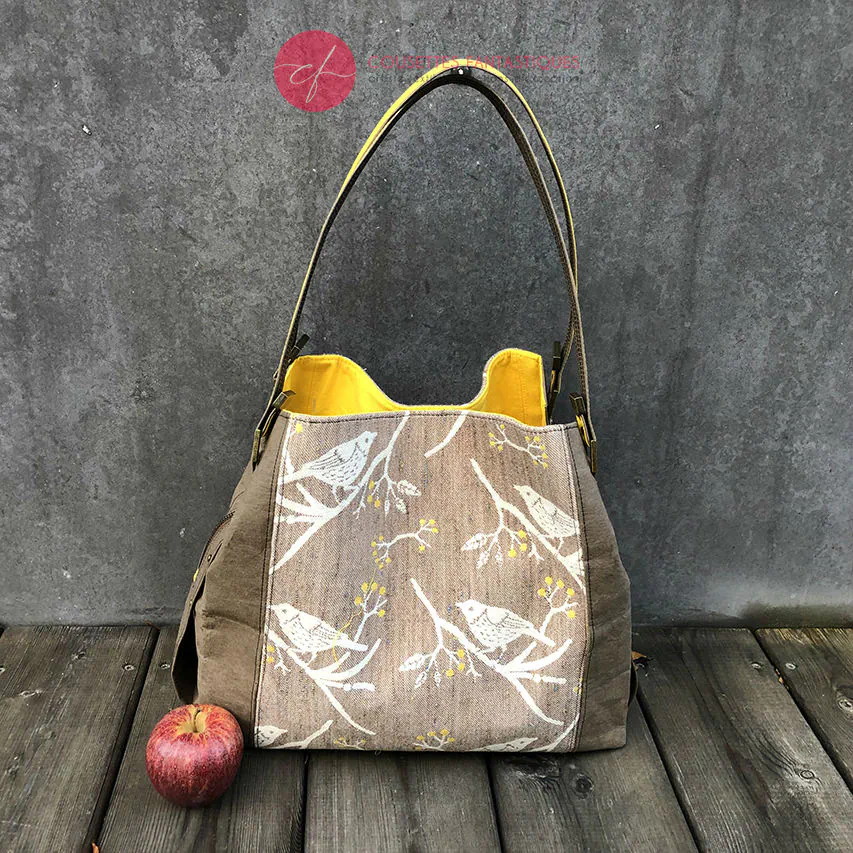 Un sac d'épaule fait à partir de papier lavable couleur chocolat, écharpe de portage beige rosé chiné, au motif d'oiseaux blancs dans des branchages blancs et jaune, avec une doublure jaune vif.