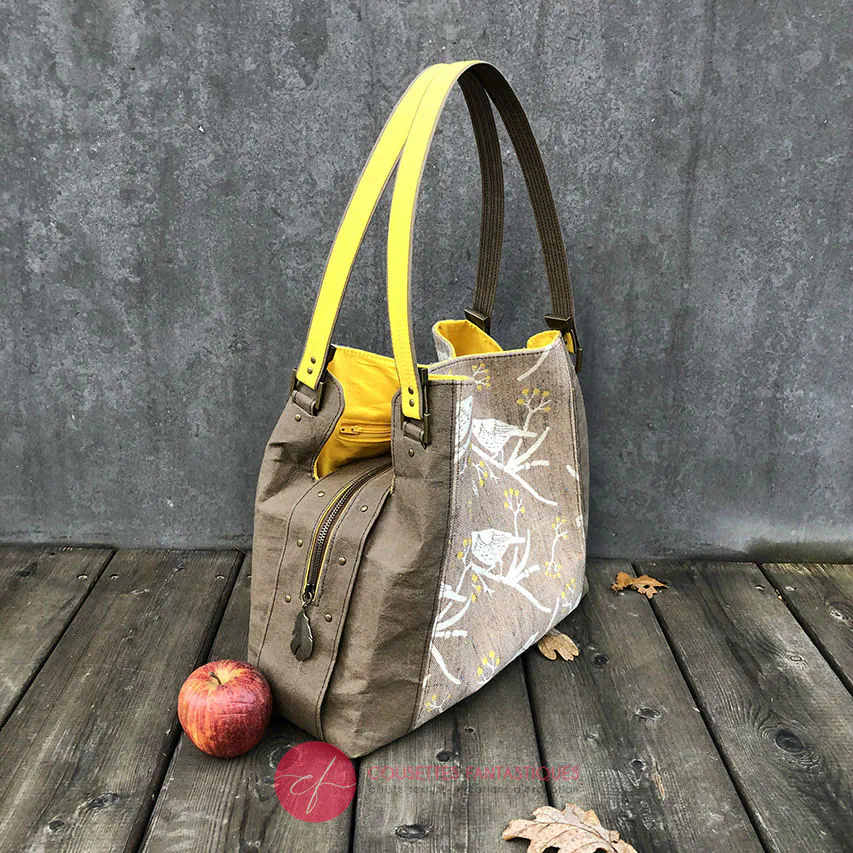 Un sac d'épaule fait à partir de papier lavable couleur chocolat, écharpe de portage beige rosé chiné, au motif d'oiseaux blancs dans des branchages blancs et jaune, avec une doublure jaune vif.