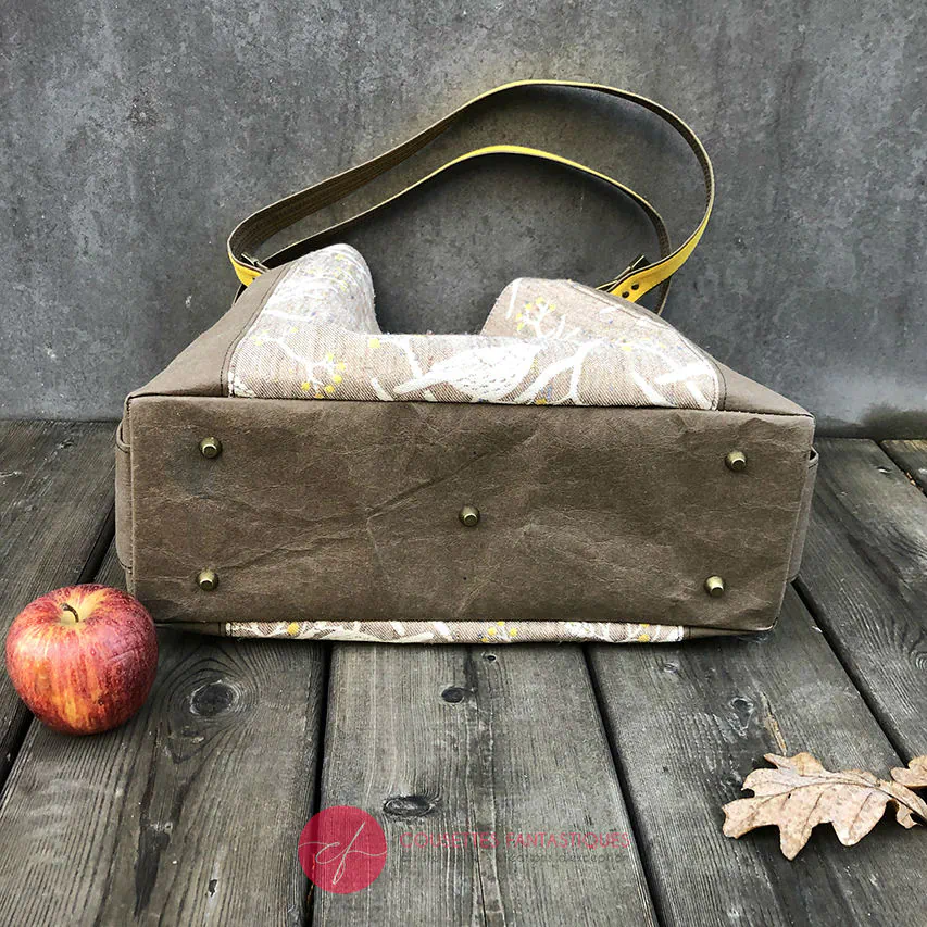 Un sac d'épaule fait à partir de papier lavable couleur chocolat, écharpe de portage beige rosé chiné, au motif d'oiseaux blancs dans des branchages blancs et jaune, avec une doublure jaune vif.