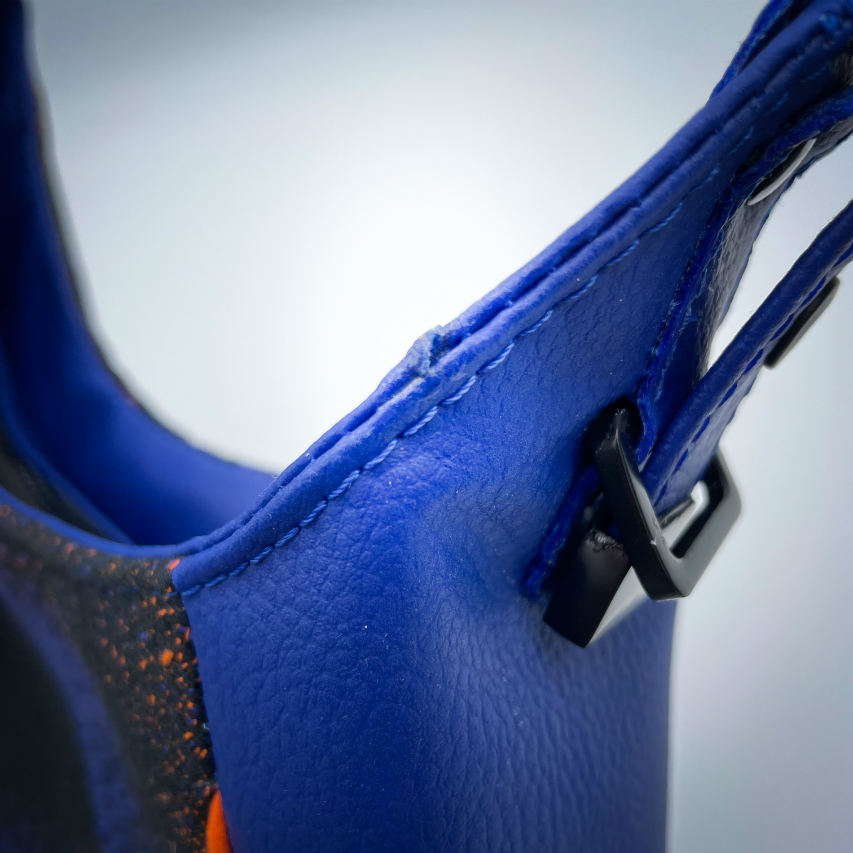 Un sac d'épaule zippé, fabriqué à partir de chutes d'une écharpe de portage noir, bleu, rose et orange et de simili bleu royal, et doublé d'une doublure orange vif lumineuse.