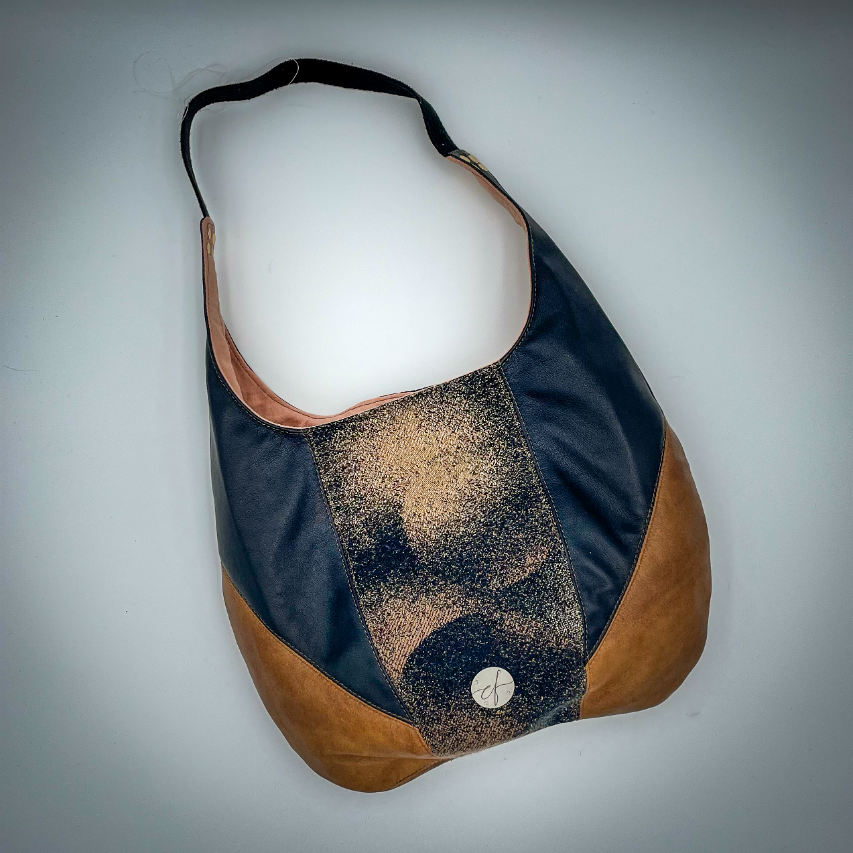 Un sac d'épaule en cuirs marron et noir, écharpe de portage noir, marron et beige avec un motif abstrait rond, et toile de lin pêche.