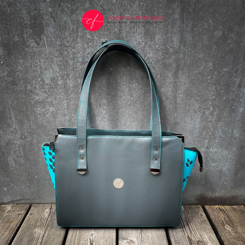 Un sac à bandoulière fabriqué à partir d'un tissu de portage turquoise avec des motifs de colibris et de pétales, associé à du similicuir gris et turquoise.