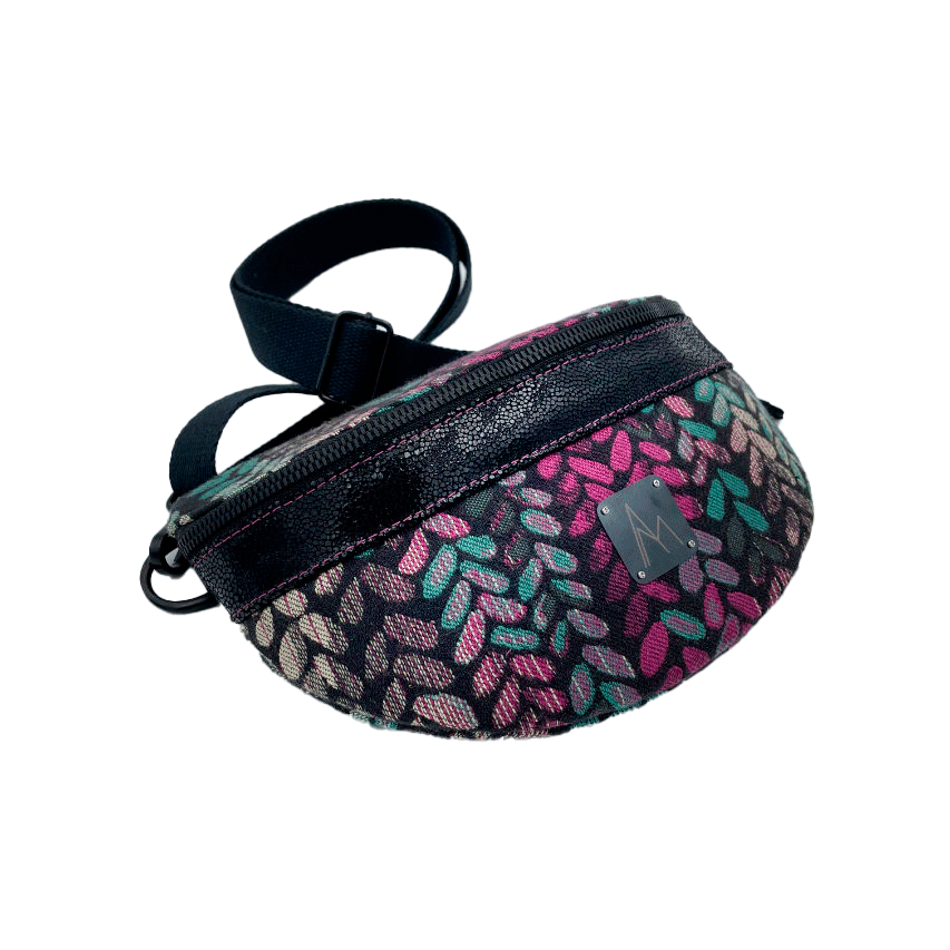 Une banane cousue dans un cuir vernis noir et une chute d'écharpe de portage au motif de mailles vertes, beiges et roses sur fond noir, couplés à une popeline rose vif à l'intérieur.