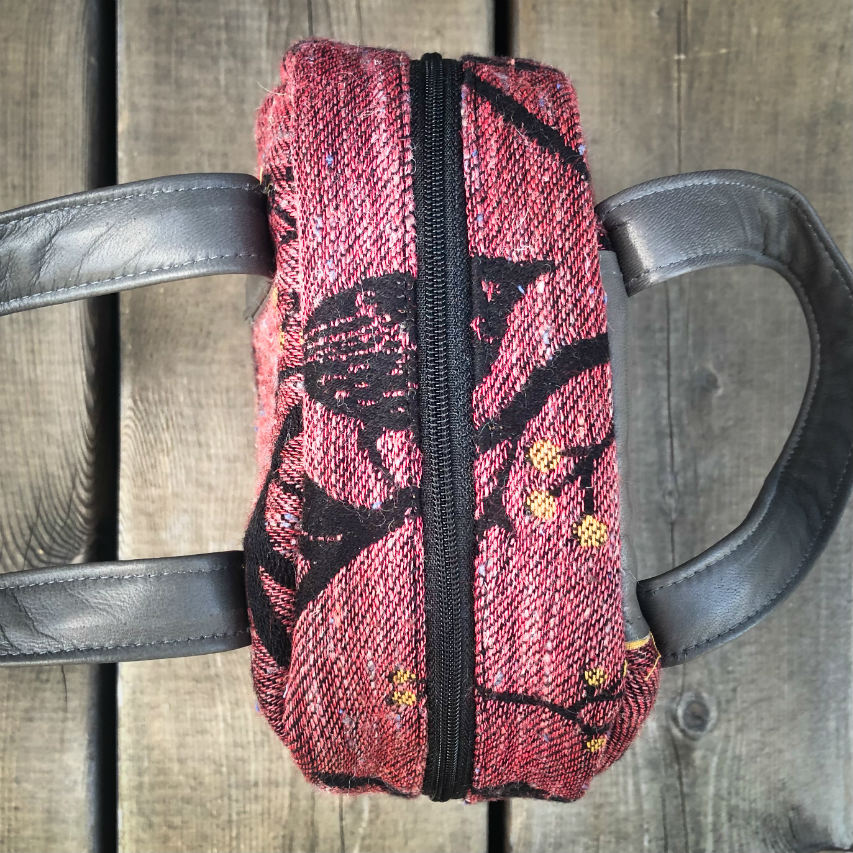 A mini handbag made of babywearing wrap scraps showing birds in a tree in pink and black tones, and grey lambskin leather.