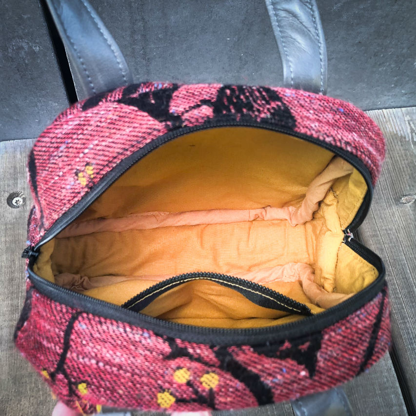 A mini handbag made of babywearing wrap scraps showing birds in a tree in pink and black tones, and grey lambskin leather.