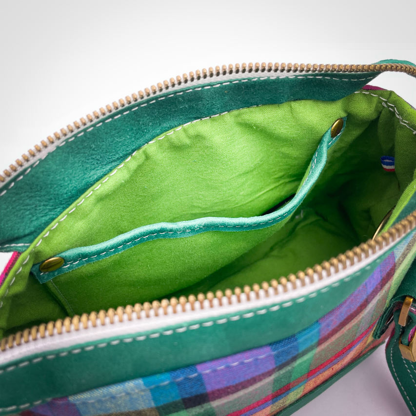 Un sac portefeuille constitué de cuir vert forêt et de toile de madras multicolore.