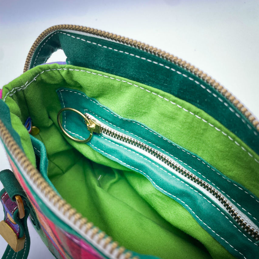 Un sac portefeuille constitué de cuir vert forêt et de toile de madras multicolore.