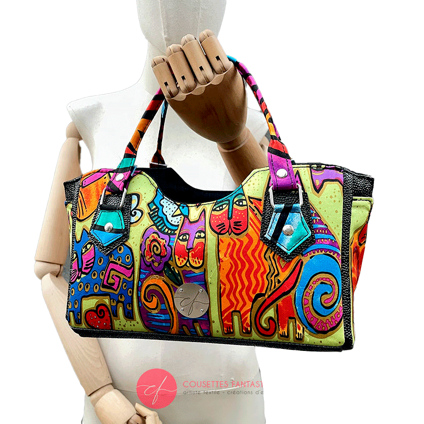 Un petit sac à main constitué d'un simili noir brillant texture galuchat et d'un foulard de soie au motif de chats très colorés.