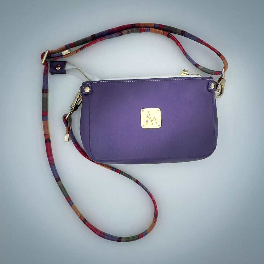 Un sac portefeuille constitué de cuir violet et de toile de madras multicolore.