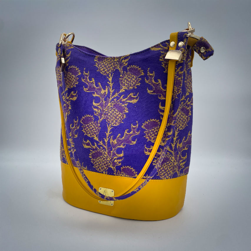 Un sac seau fabriqué avec de l'écharpe de portage au motif de chardons jaunes sur fond violet et du cuir d'agneau jaune.