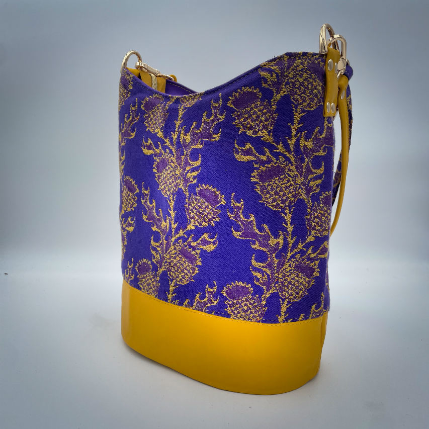 Un sac seau fabriqué avec de l'écharpe de portage au motif de chardons jaunes sur fond violet et du cuir d'agneau jaune.