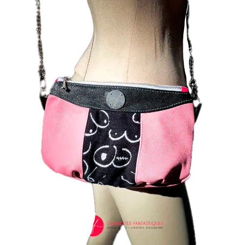 Un sac en bandoulière fabriqué à partir d'une écharpe de portage noir et blanc avec des dessins stylisés de seins, et de cuirs type galuchat en noir et rose.
