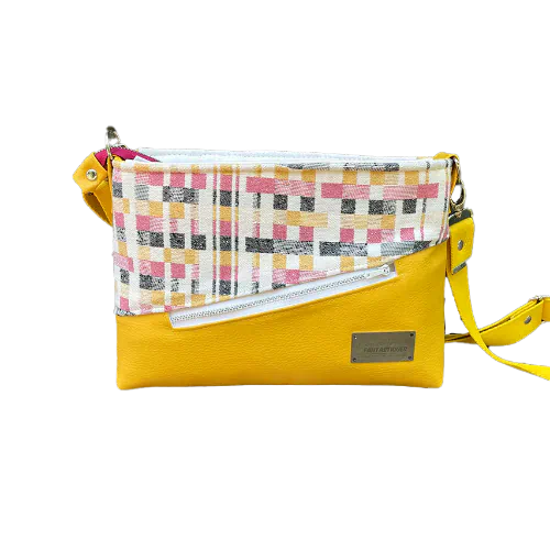 Un sac à bandoulière rectangulaire fabriqué à partir d'écharpe de portage noir, blanc, rose et jaune à motif géométrique, et de simili jaune tournesol.