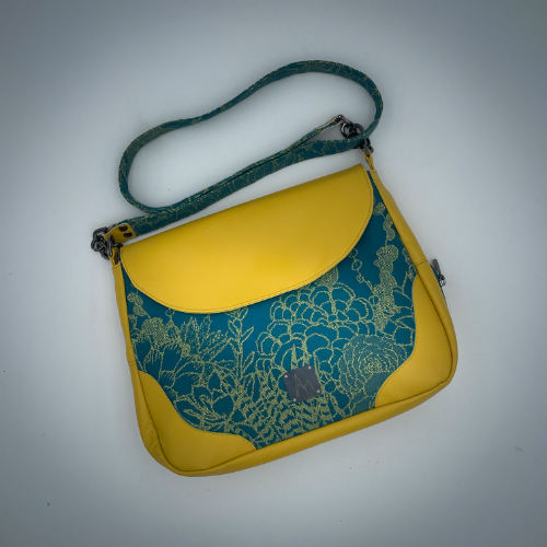 Un sac besace confectionné à partir d'écharpe de portage au motif de succulentes jaunes sur fond turquoise et d'un cuir jaune soleil, couplés à deux popelines bleu glace et jaune à l'intérieur.