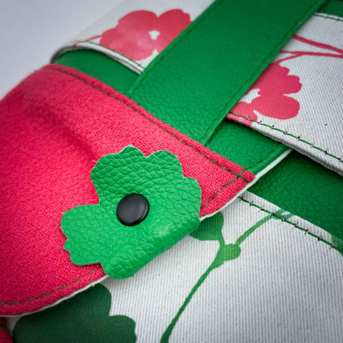 Un sac en bandoulière fabriqué à partir de néoprène aux motifs floraux, d'un crêpe rose fuschia et de cuir grainé vert vif.