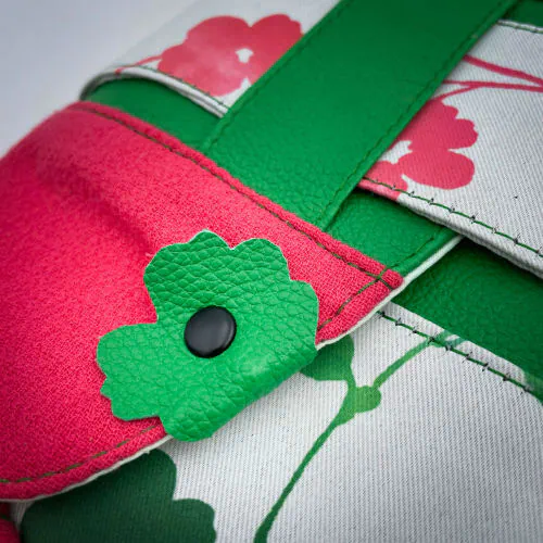 Un sac en bandoulière fabriqué à partir de néoprène aux motifs floraux, d'un crêpe rose fuschia et de cuir grainé vert vif.