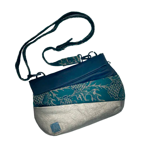 Un sac d'épaule constitué à l'extérieur de deux cuirs doré et noir et d'un coupon d'écharpe de portage noir, vert et doré au motif de chardons, et à l'intérieur de popeline vert forêt et de satin doré.