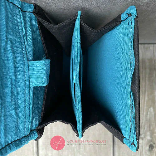 Un portefeuille-sac fabriqué à partir d'une écharpe de portage grise, noir et bleu ciel avec des motifs stylisés de tête de moineau, et du liège noir.