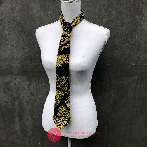 Une cravate fabriquée à partir d'un tissu d'écharpe de portage noir et or au motif marbré.