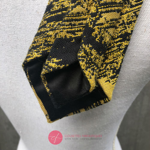 Une cravate fabriquée à partir d'un tissu d'écharpe de portage noir et or au motif marbré.