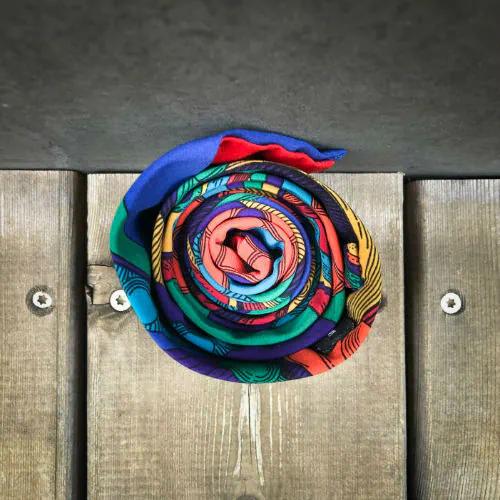Une cravate fabriquée à partir d'un foulard de soie rouge, bleu, vert, jaune... et au motif rococco.