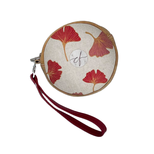 Une pochette ronde faite de cuir de couleur camel et d'une toile en polycoton avec un motif de feuilles de Ginkgo Biloba rouges.