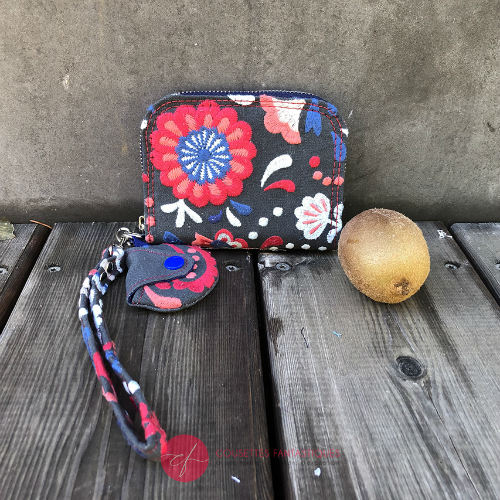 A small zippered card and coin holder made of gray fabric embroidered with blue, red, and white Scandinavian floral patterns.
