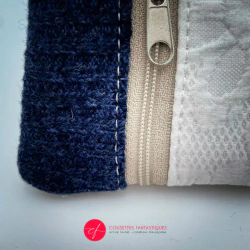 Un petit porte-monnaie zippé fabriqué à partir d'un pull en laine bleu marine, d'un tissu damassé blanc et d'un simili suédé beige.
