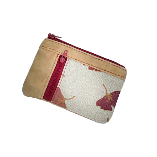 Un mini portemonnaie zippé fait de cuir de couleur camel et d'une toile en polycoton avec un motif de feuilles de Ginkgo Biloba rouges.
