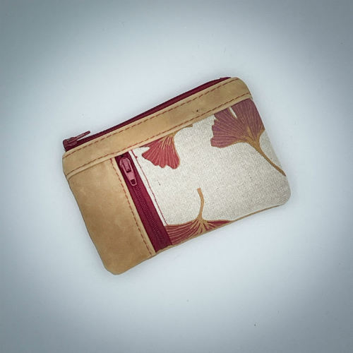 Un mini portemonnaie zippé fait de cuir de couleur camel et d'une toile en polycoton avec un motif de feuilles de Ginkgo Biloba rouges.