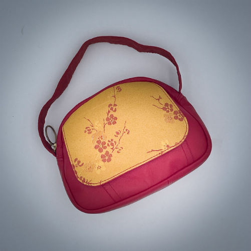 Un mini sac à main constitué de tissu d'ameublement jaune motif fleurs de cerisier rouge et de cuir rouge.