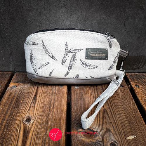 A small zippered pouch sewn in gray faux leather and a white and gray babywearing wrap with a feather pattern.